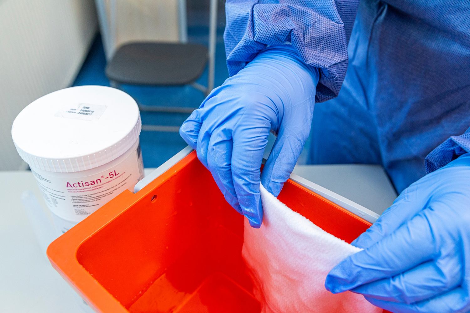 Een schoonmaker met beschermende kleding aan bereid een doekje voor met een oplossing van Actisan
