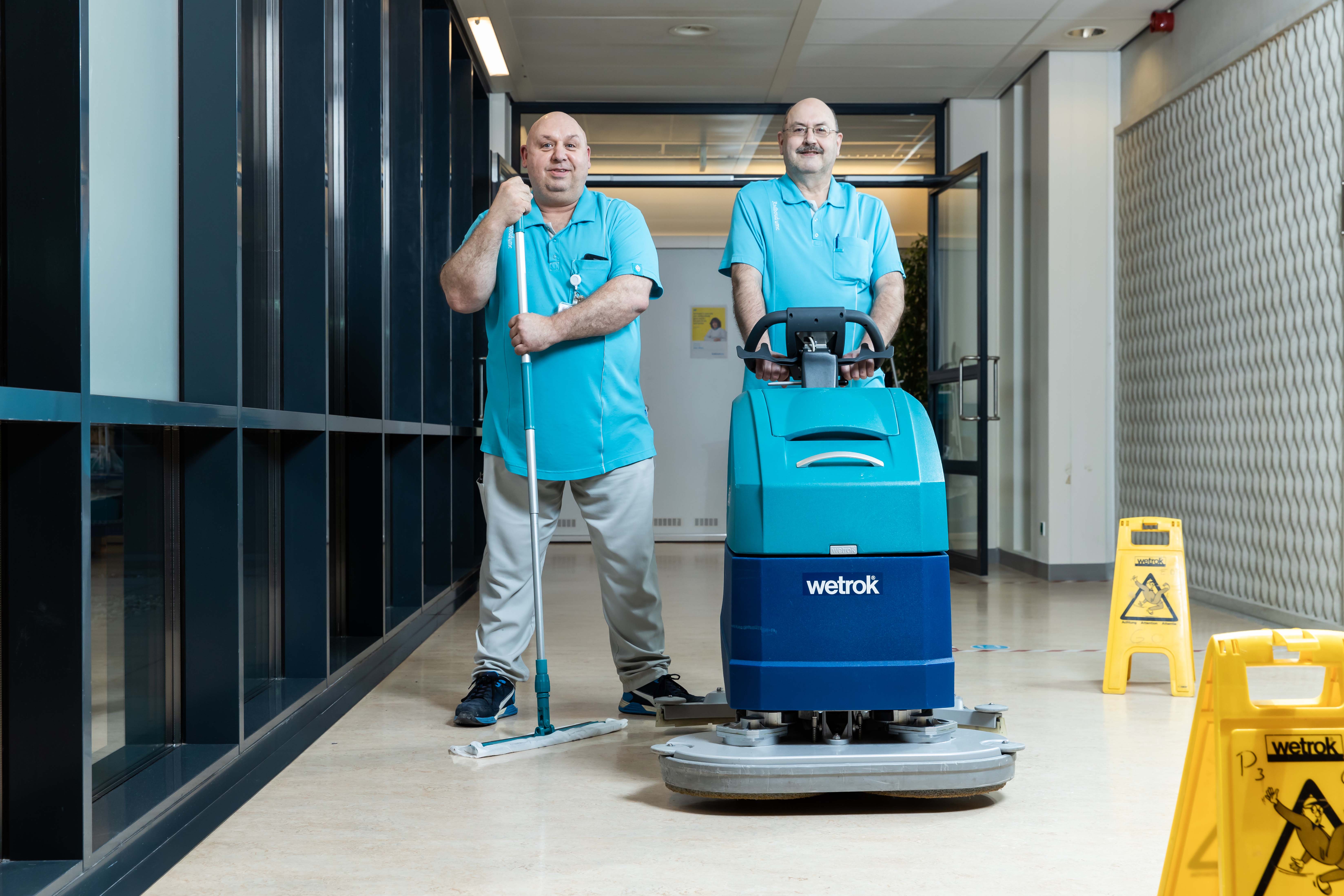 twee trotse vloerspecialisten in de hal met hun machines